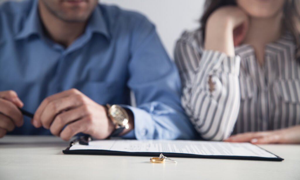 Couple signant un accord de divorce par consentement mutuel avec leurs alliances posées sur la table.